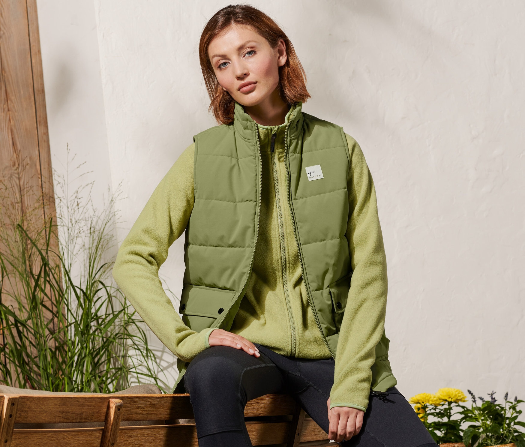 Kadın bir bankta oturuyor ve kapitone yelek giyiyor.