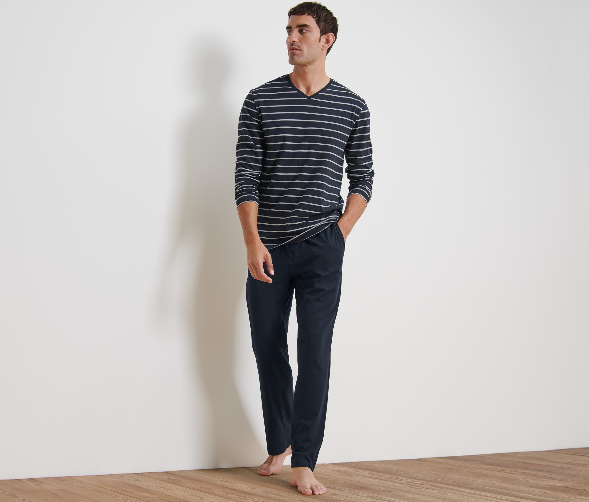 Ayakta duran bir adam pijama giyiyor. Uzun kollu, çizgili bir üst ve lacivert bir pantolondan oluşuyor.