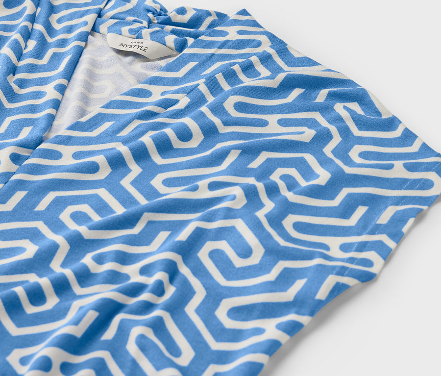 Mavi renkli, V yakalı, beyaz geometrik desenli bluzun yakın çekimi.
