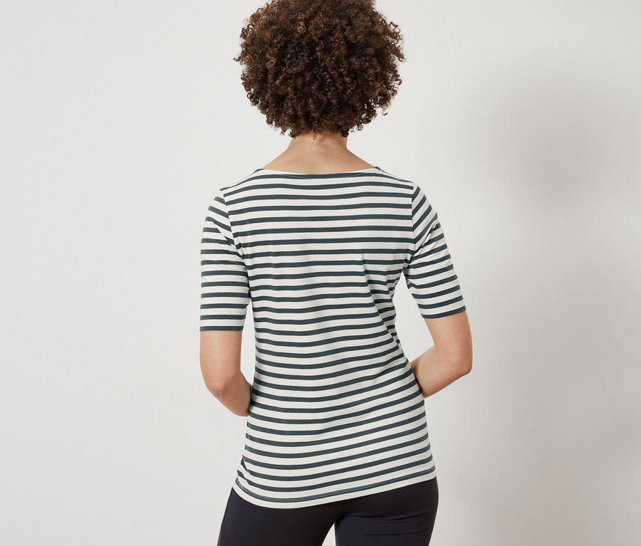 Kahverengi kıvırcık saçlı, yeşil çizgili, yarım kollu bir tişört ve siyah pantolon giyen bir kadının arka görünümü.