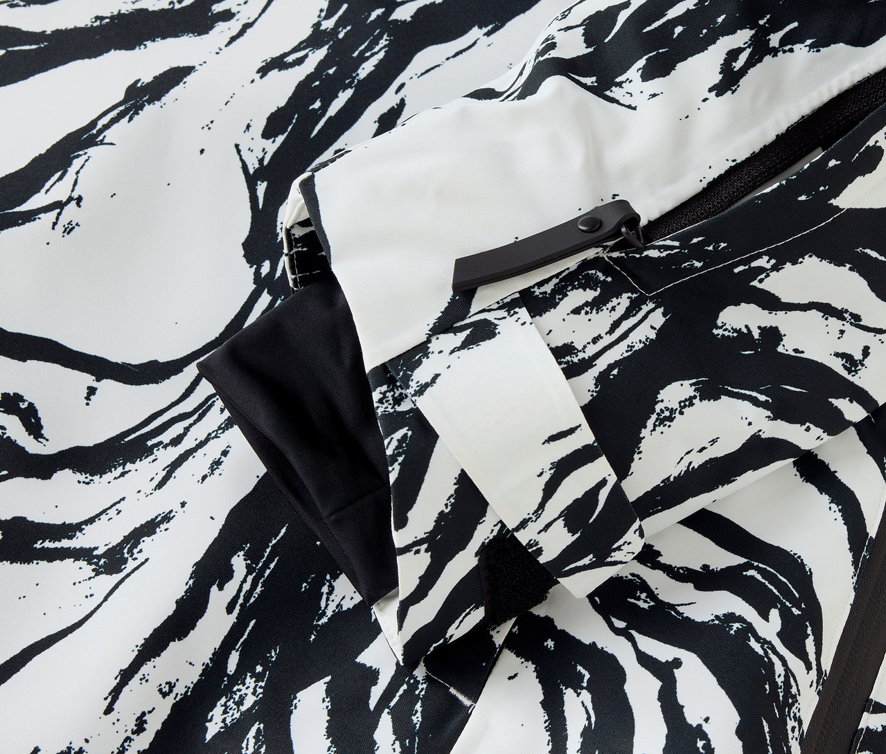 Beyaz ve siyah renklerde zebra desenli bir ceket detayı, kol ve fermuarı görülebilir.