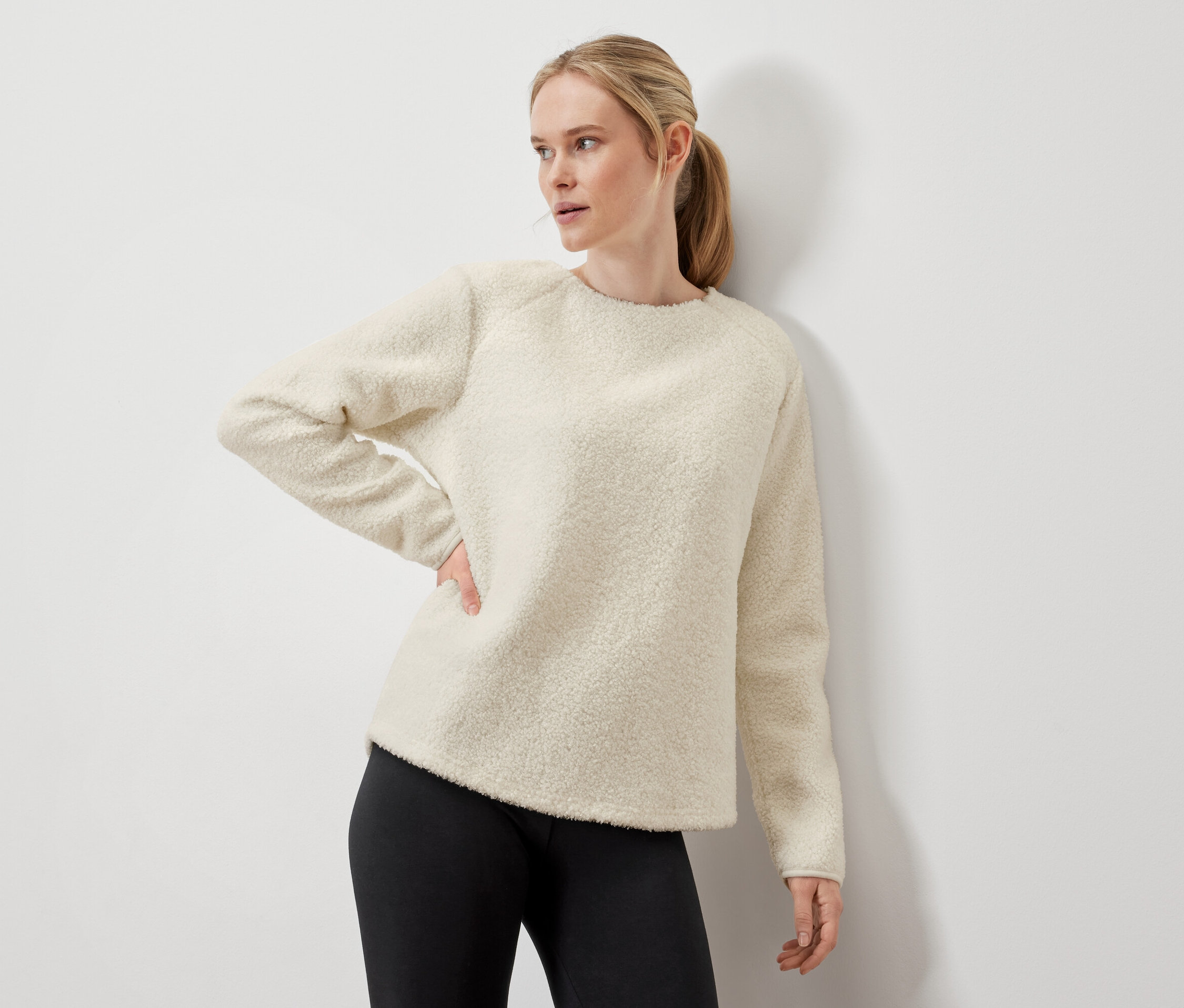 Krem rengi bir kazak ve siyah tayt giyen bir kadın poz veriyor.