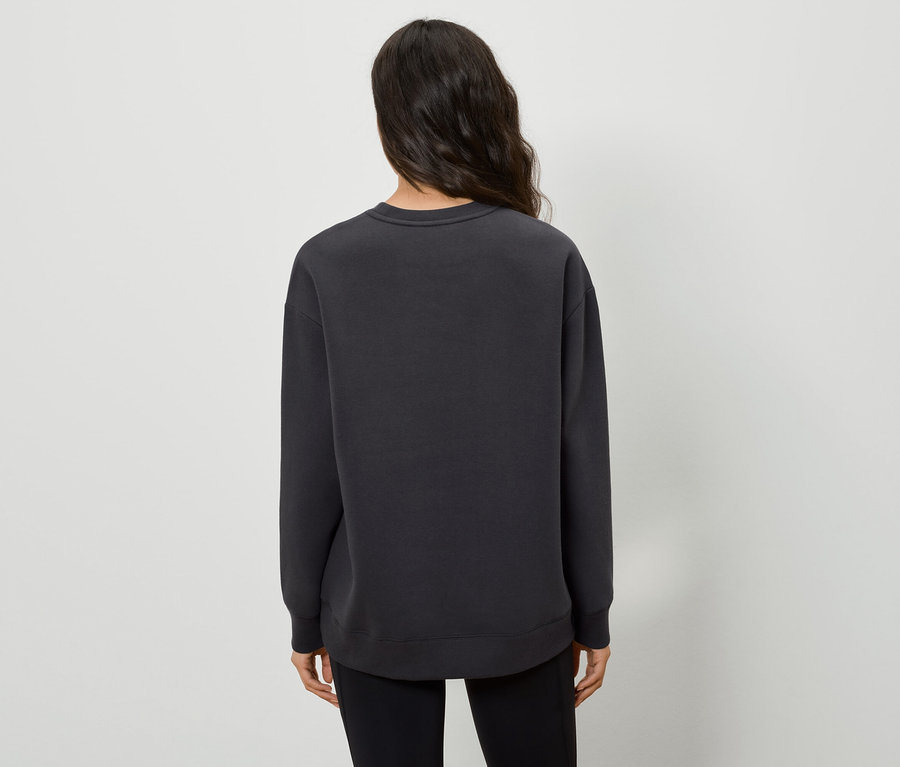 Siyah bir kazak ve siyah pantolon giyen koyu saçlı bir kadının arka görünümü.