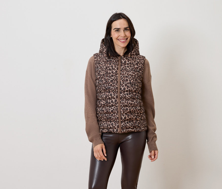 Kahverengi kapüşonlu, hayvan desenli bir yelek ve kahverengi deri pantolonlu bir kadın poz veriyor.