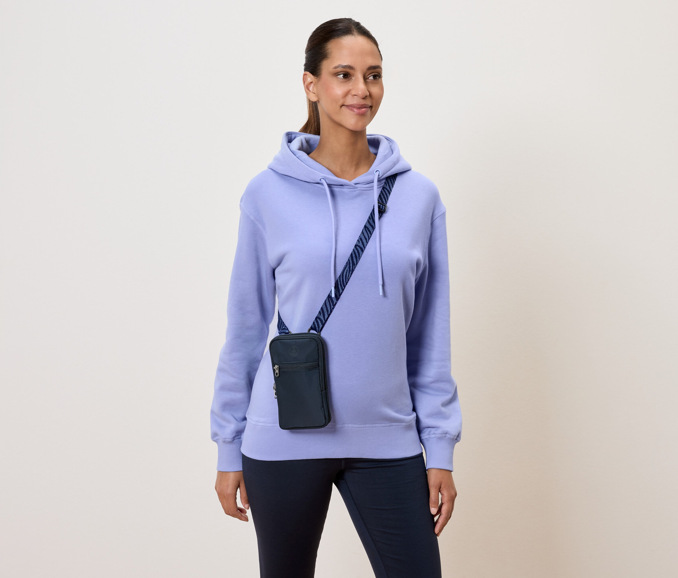 Kadın açık mor kapüşonlu sweatshirt ve lacivert omuz çantası takıyor.