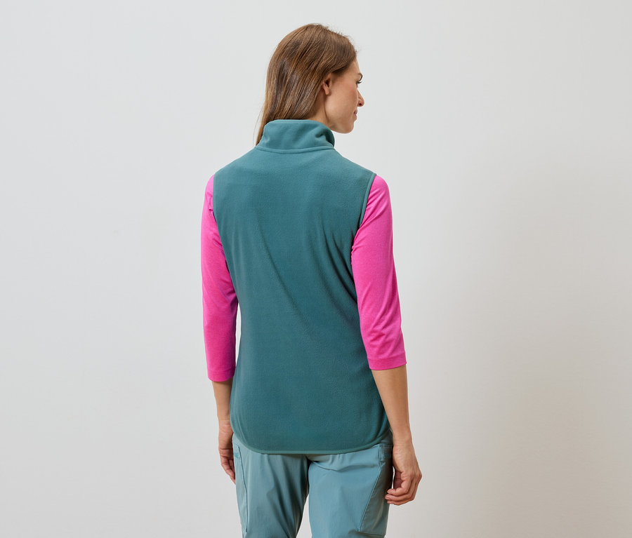 Uzun kahverengi saçlı, turkuaz renkli polar yelek, pembe uzun kollu tişört ve turkuaz pantolon giyen bir kadının arka görünümü.