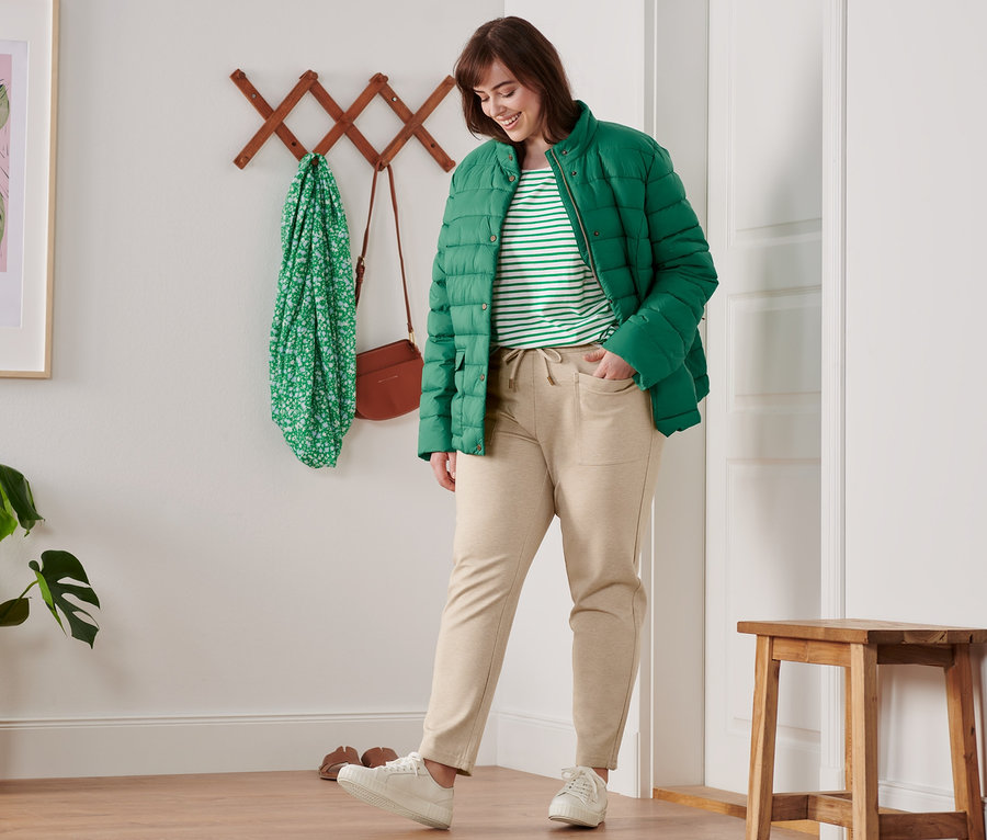 Kadın yeşil kapitone mont, çizgili 3/4 kol tişört ve jogger pantolon giyiyor.