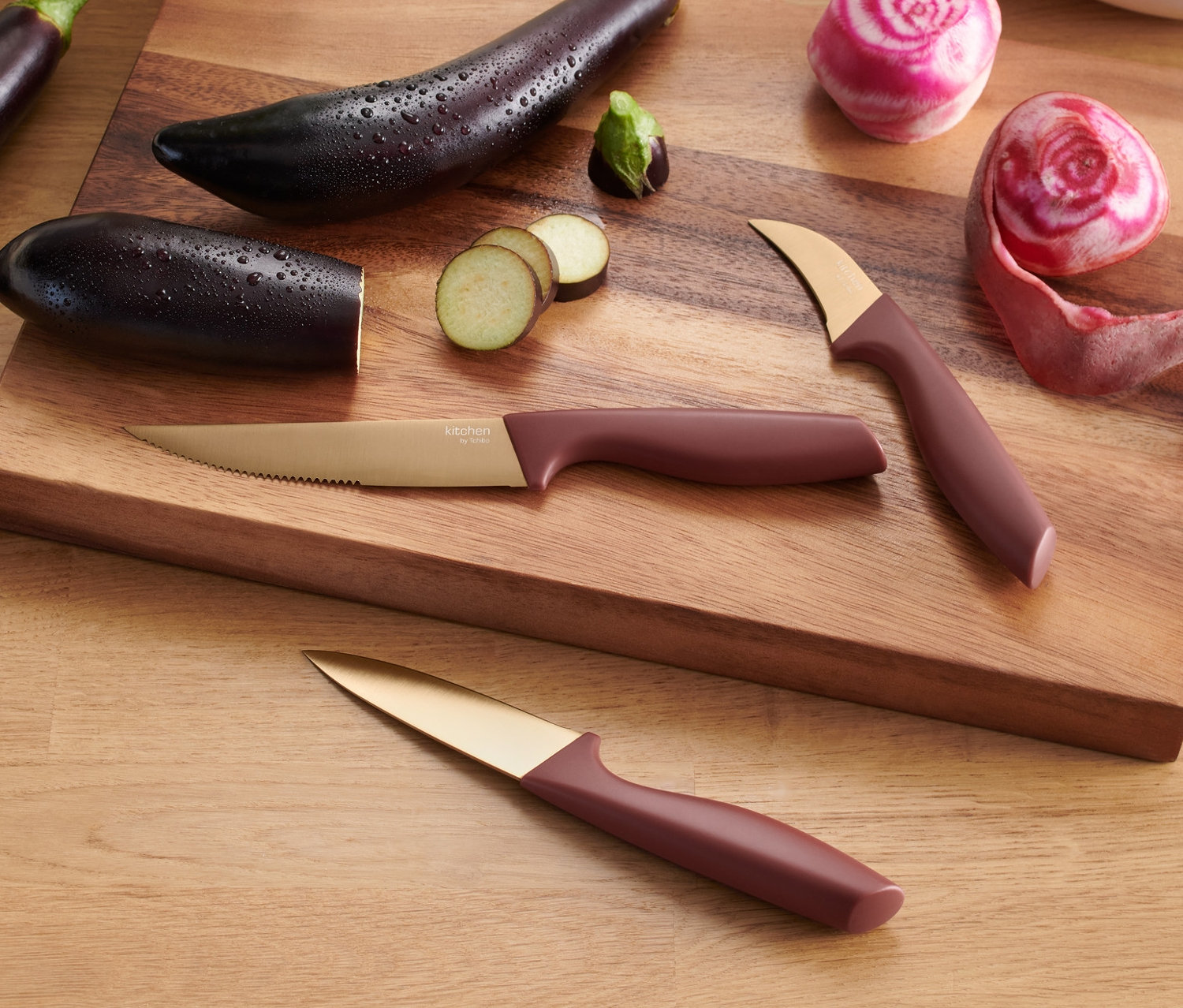 Ahşap kesme tahtası üzerinde üç adet patlıcan, kesilmiş pancar ve 3 adet mutfak bıçağı bulunmaktadır.