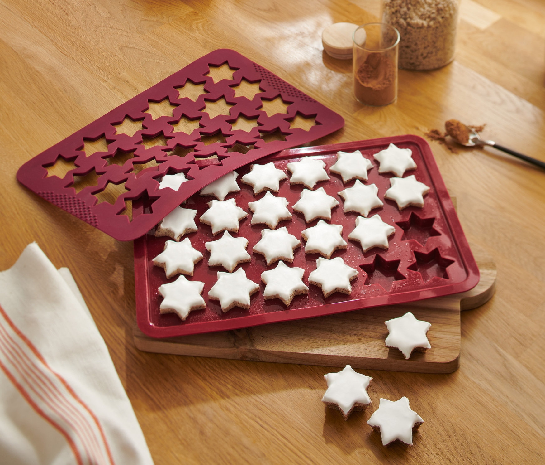 Ahşap bir masanın üzerinde pişmiş yıldızlarla birlikte kırmızı bir Yıldız Kurabiye Fırın Matı duruyor.