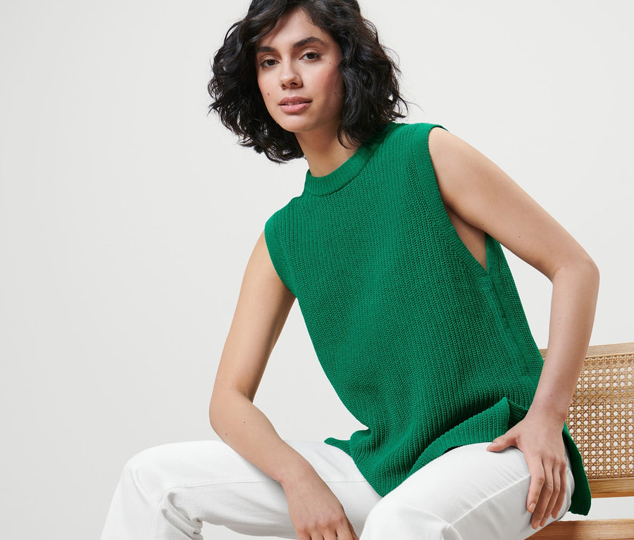 Kadın sandalyede oturuyor ve yeşil, Kalın Örgü Kolsuz Süveter giyiyor.