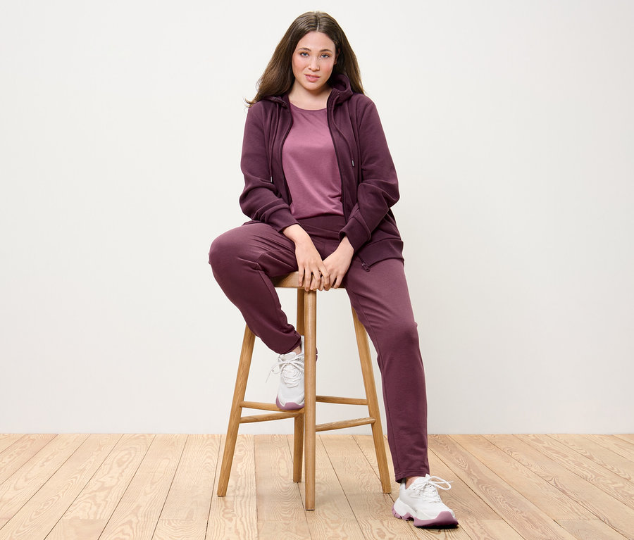 Bir kadın sandalyede oturuyor; üzerinde Sweat Ceket ve Mürdüm rengi Sweat Pantolon var.