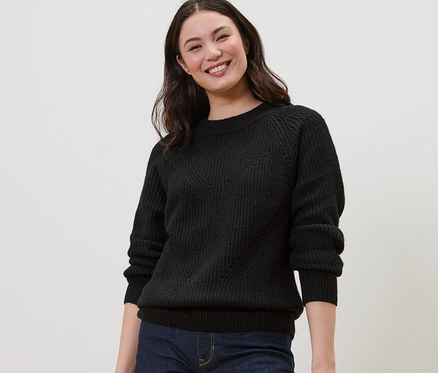 Gülümseyen kadın siyah örgü kazak giyiyor.