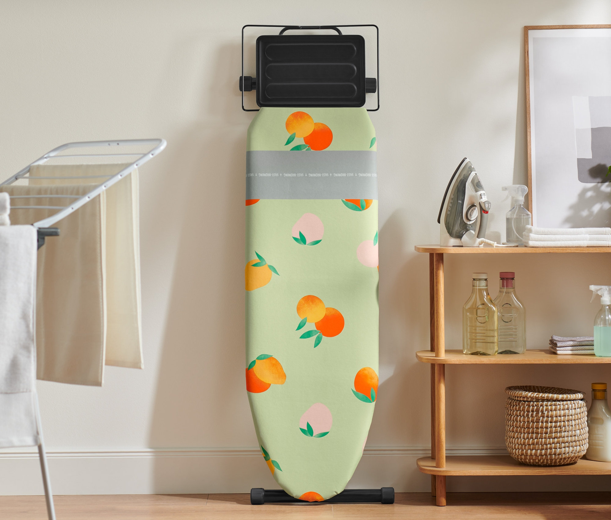 Şeftali desenli ütü masası kılıfı olan bir ütü masası duvara yaslanmış.