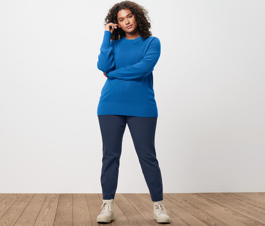 Kadın İnce Örgülü Kazak, Koyu Mavi Streç Pantolon ve deri spor ayakkabılarıyla poz veriyor.