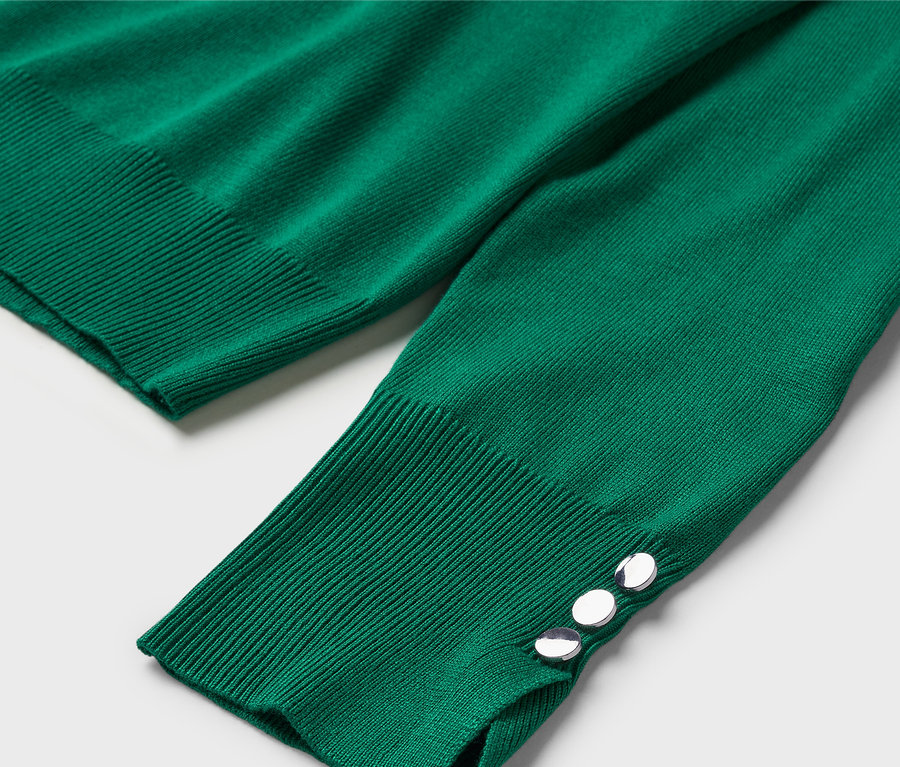 Manşetinde dekoratif düğmeler bulunan, uzun kollu yeşil bir kazağın yakın çekimi.