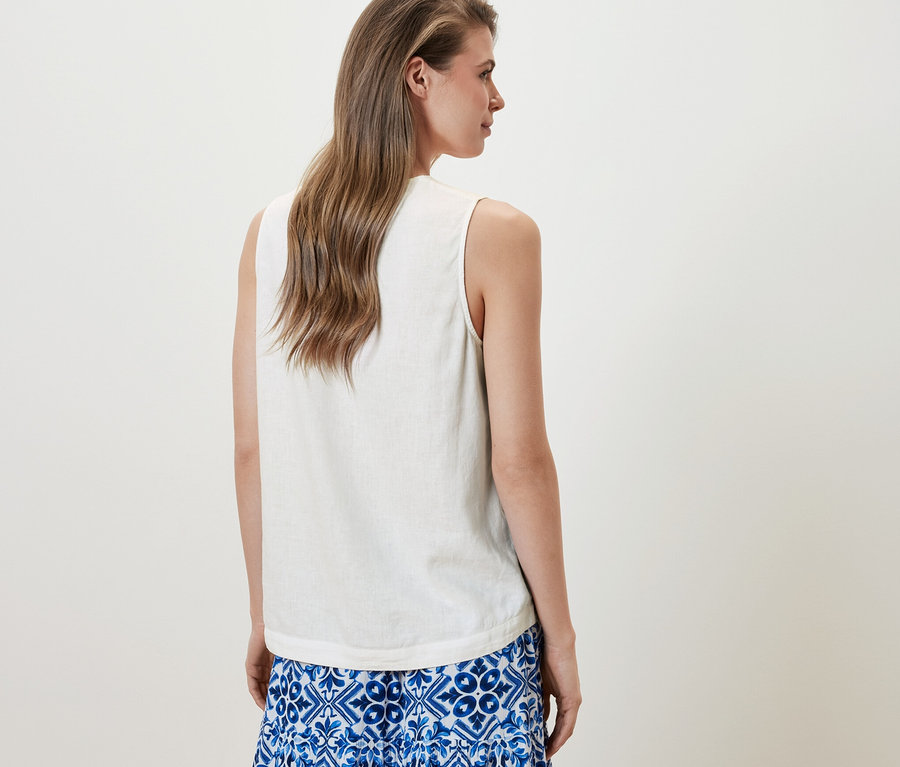 Kadın, Beyaz Kolsuz Keten Bluz ve mavi bir etek giyiyor.