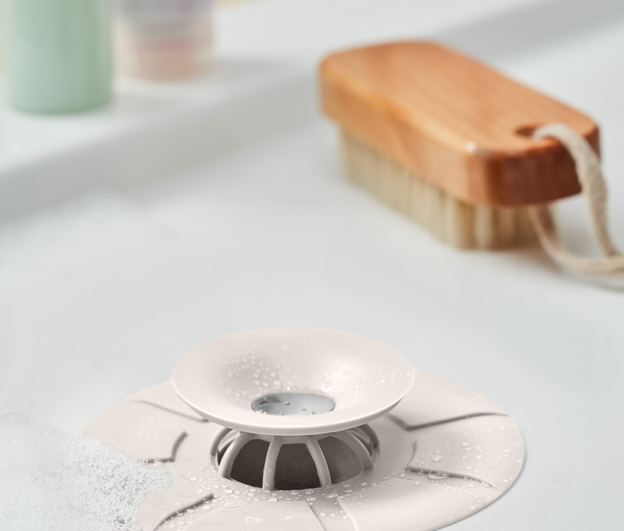 Lavabonun ortasında beyaz bir kir tutucu detayı. Arka planda fırça ve şişeler bulunuyor.