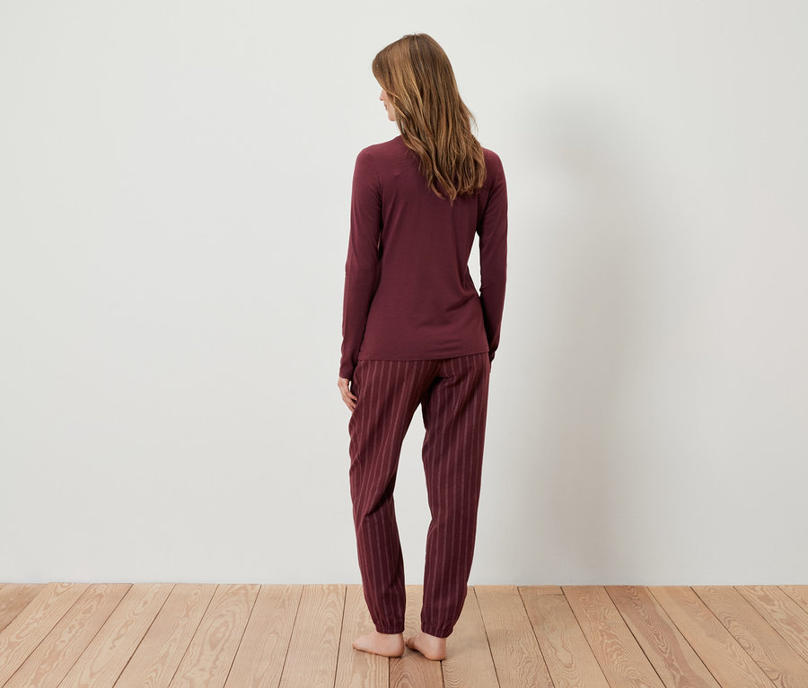 Kadın kameraya arkası dönük duruyor ve bordo bir pijama giyiyor.