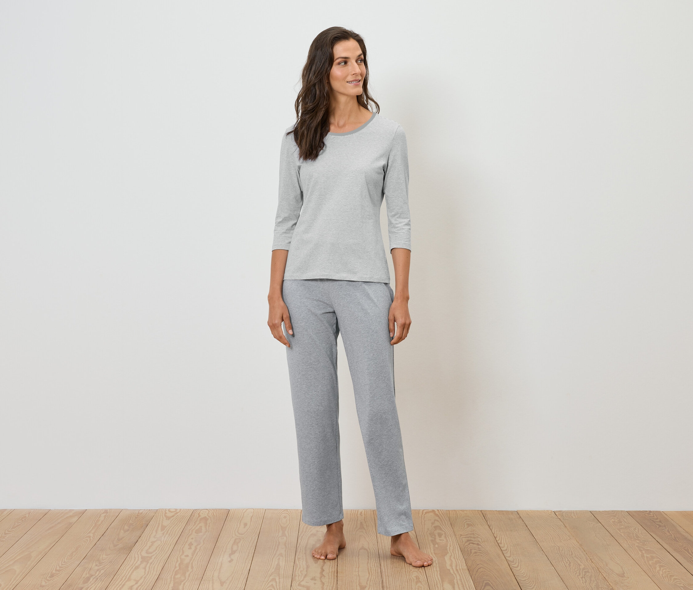 Gri pijama giyen bir kadın ayakta duruyor.