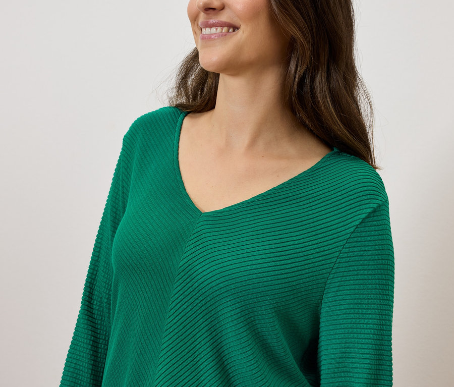 Kahverengi saçlı, gülen bir kadın, yeşil V yakalı bir kazak giyiyor.