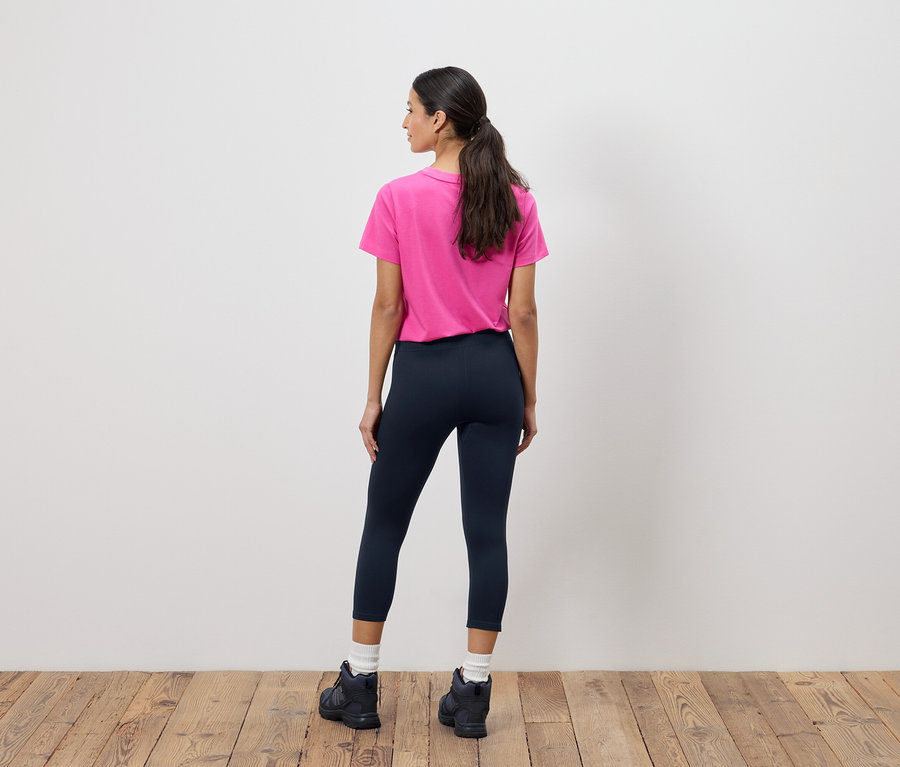 Atkuyruklu, pembe tişörtlü, lacivert taytlı ve siyah botlu bir kadının arka görüntüsü.