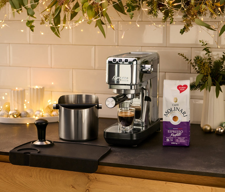 Mutfak tezgahında, bir fincan espressonun yanında gümüş renkli »Lapressa« Portafiltre Makinesi duruyor.