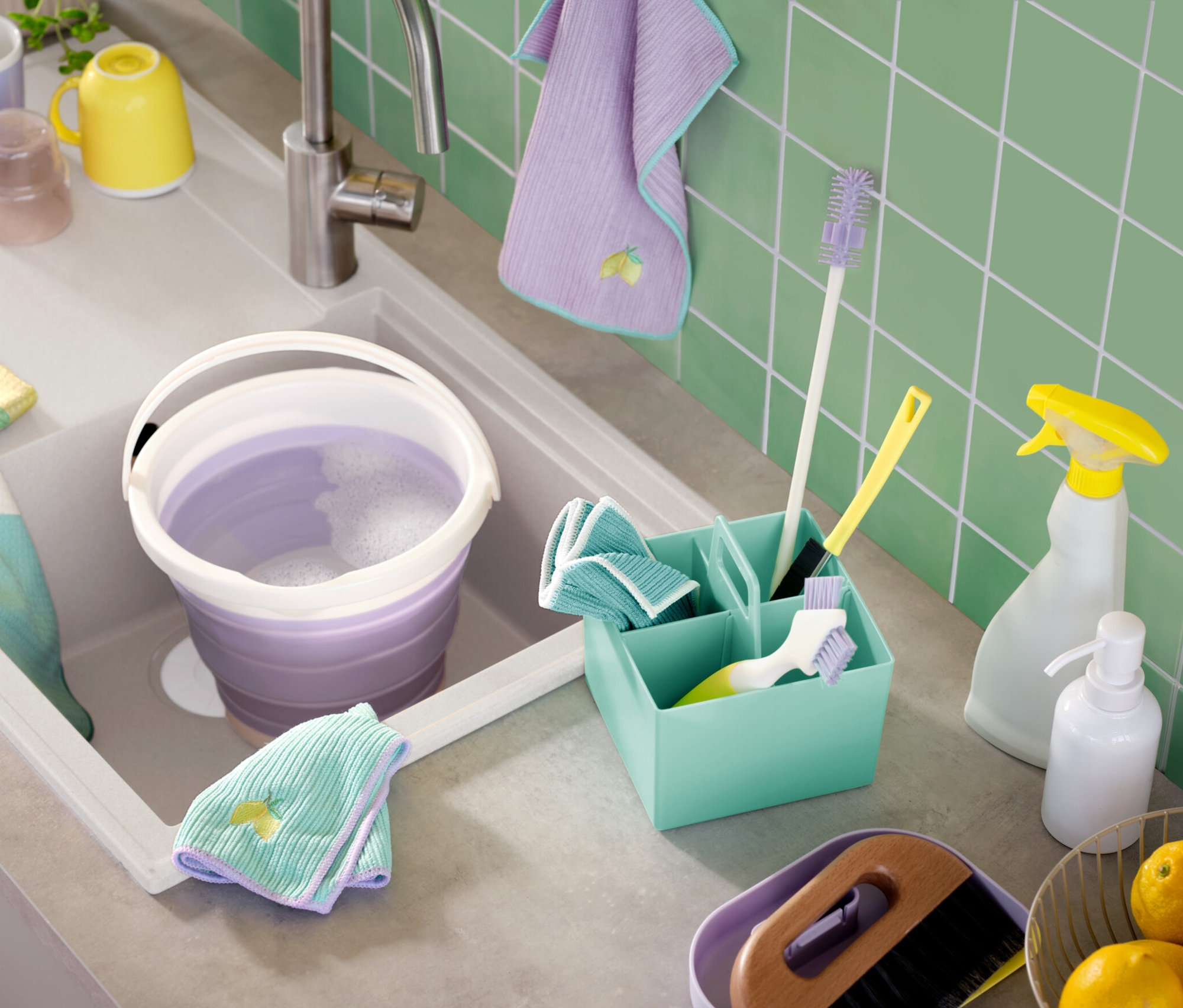 Lavaboda sabunlu su bulunan mor bir kova, etrafında fırçalar, spreyler ve bezler gibi temizlik malzemeleri bulunmaktadır.