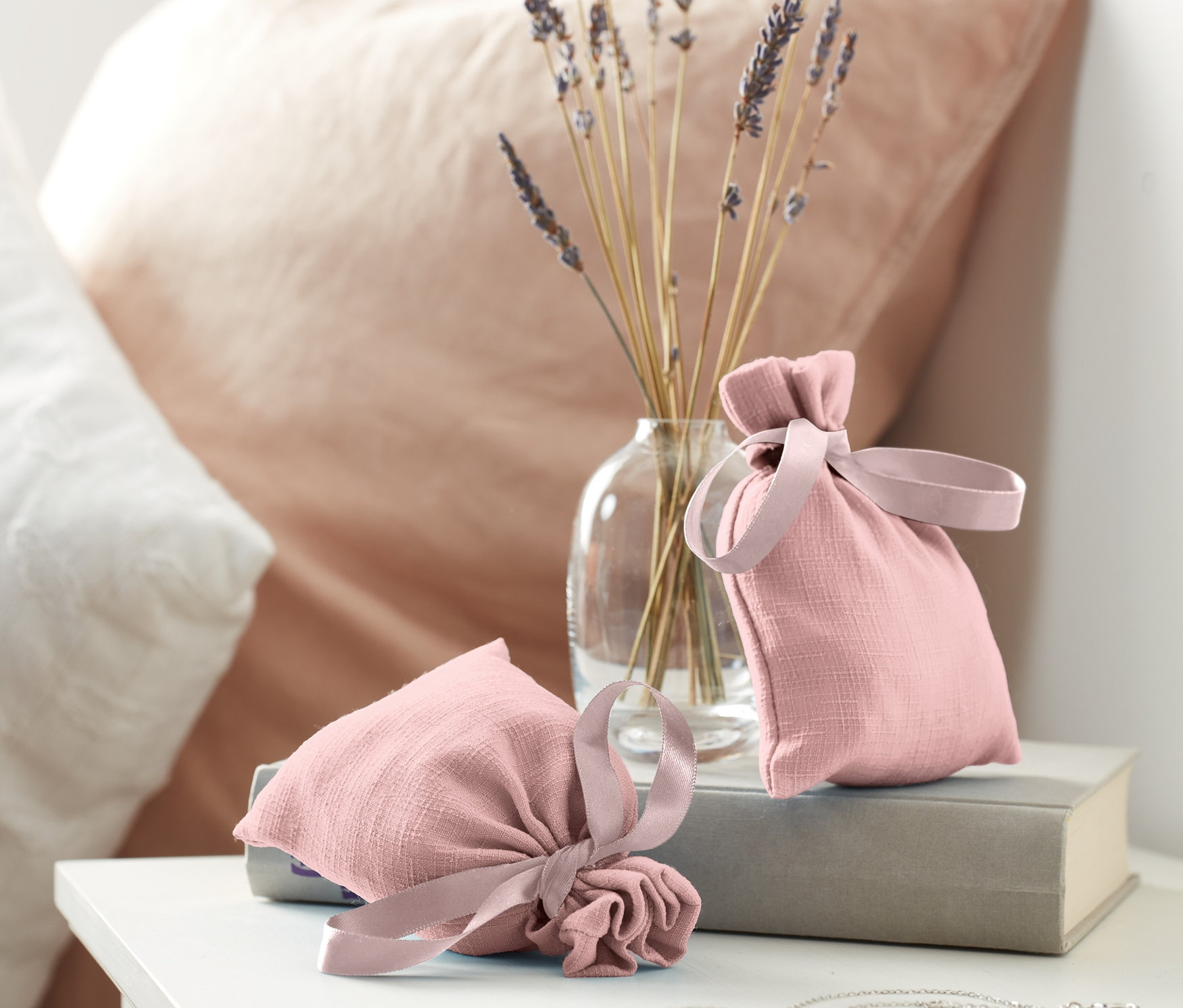 İki adet koku kesesi, lavanta dolu bir vazonun yanında bir kitabın üzerinde duruyor.