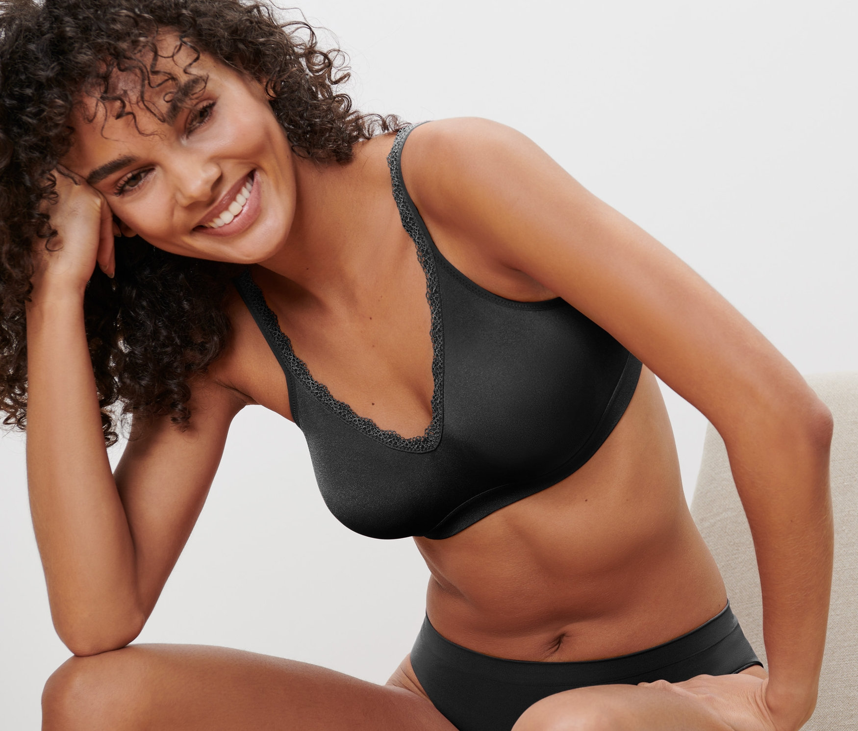 Sandalyede oturan gülümseyen bir kadın, üzerinde Siyah Dikişsiz Yumuşak Sütyen var.