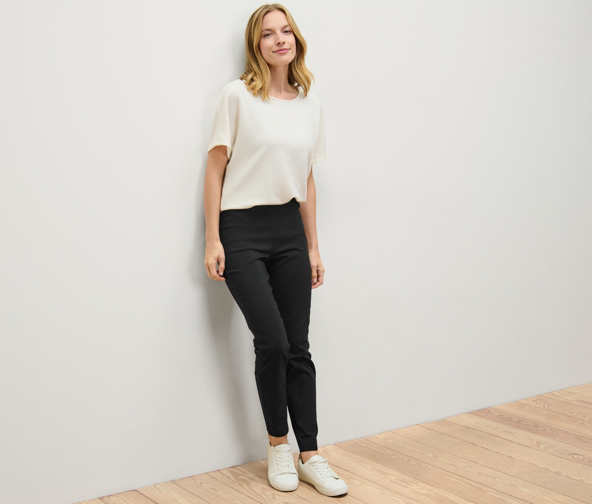 Duvara yaslanmış bir kadın siyah streç pantolon giyiyor.