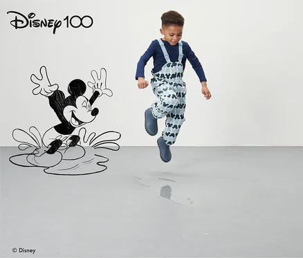 Oğlan, Mickey Mouse desenli mavi Küçük Çocuk Termal Yağmur Pantolonu »Micky« ile gri zeminde zıplıyor.
