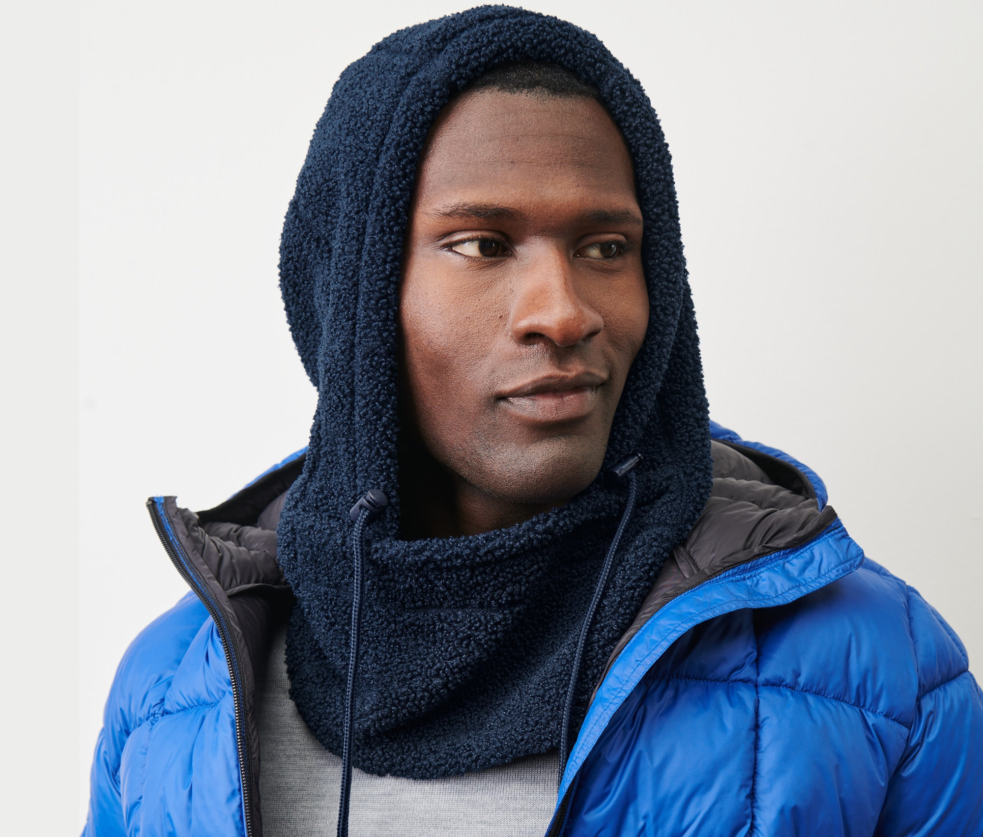 Adam, Dik Yakalı Teddy Kapüşon ve mavi şişme mont giyiyor.