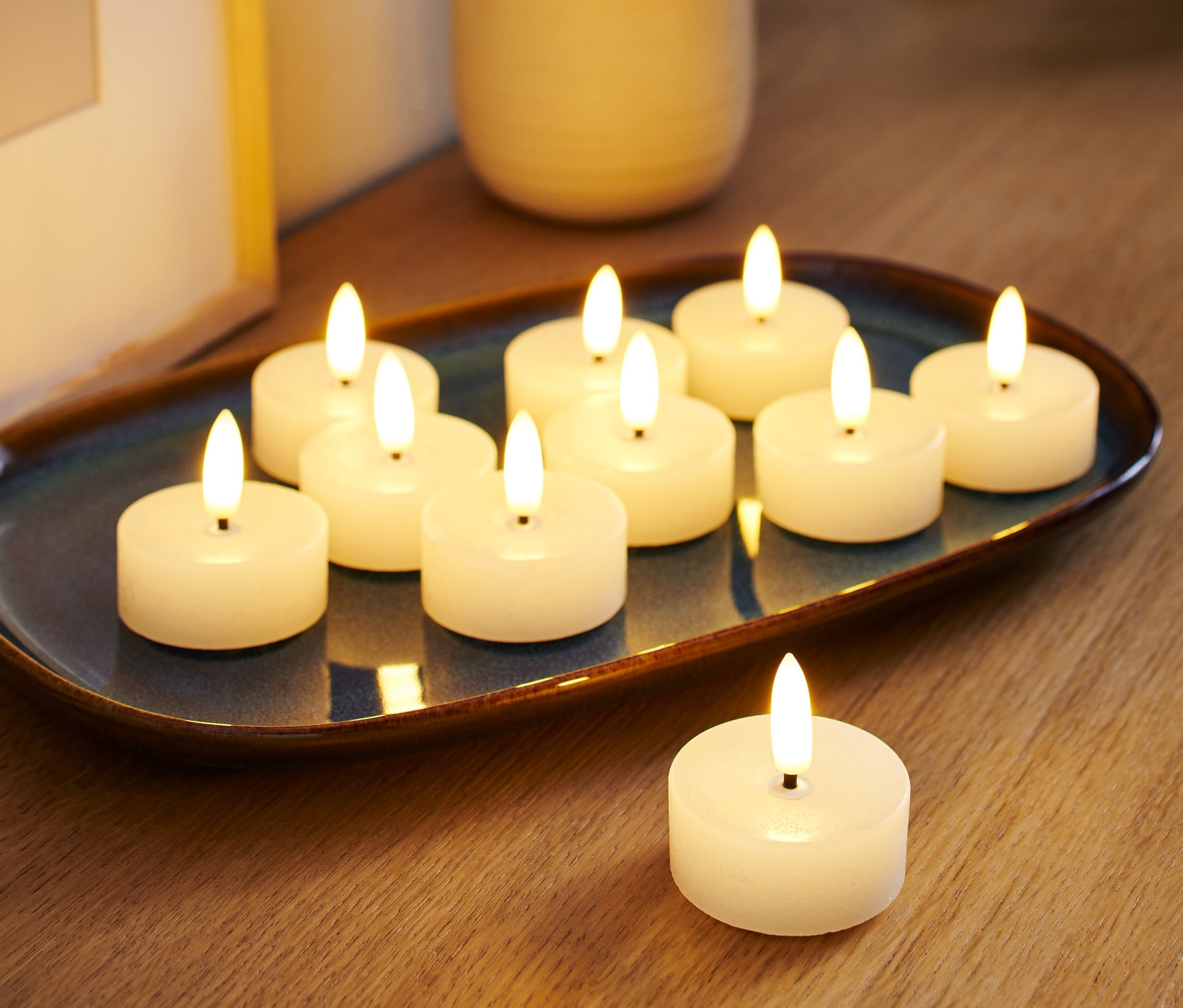 Mavi bir tabakta on adet beyaz LED tealight mum bulunuyor, bir adet tealight mum da yanında duruyor.