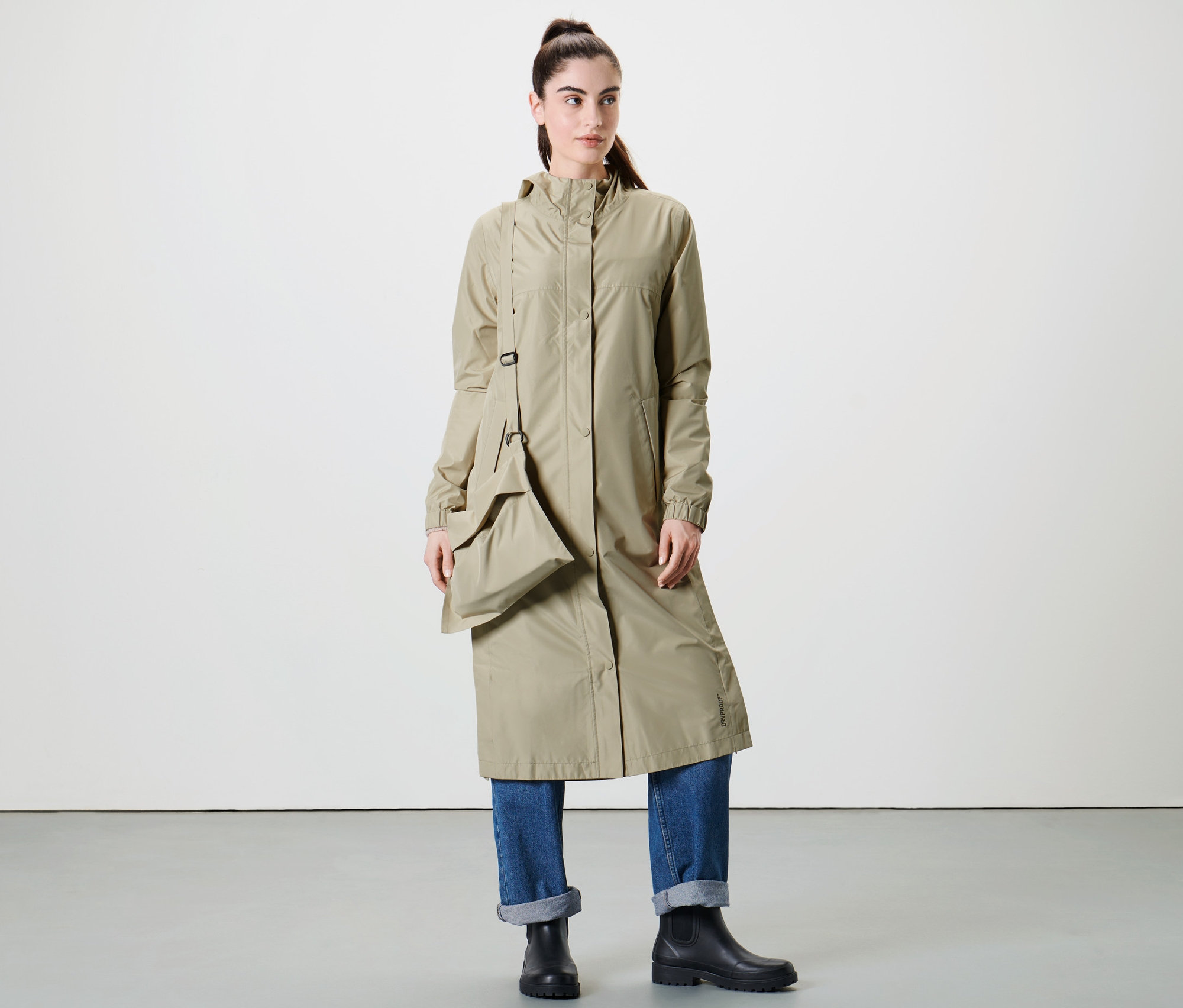 Kadın stüdyoda ekstra uzun bej yağmur montuyla poz veriyor.