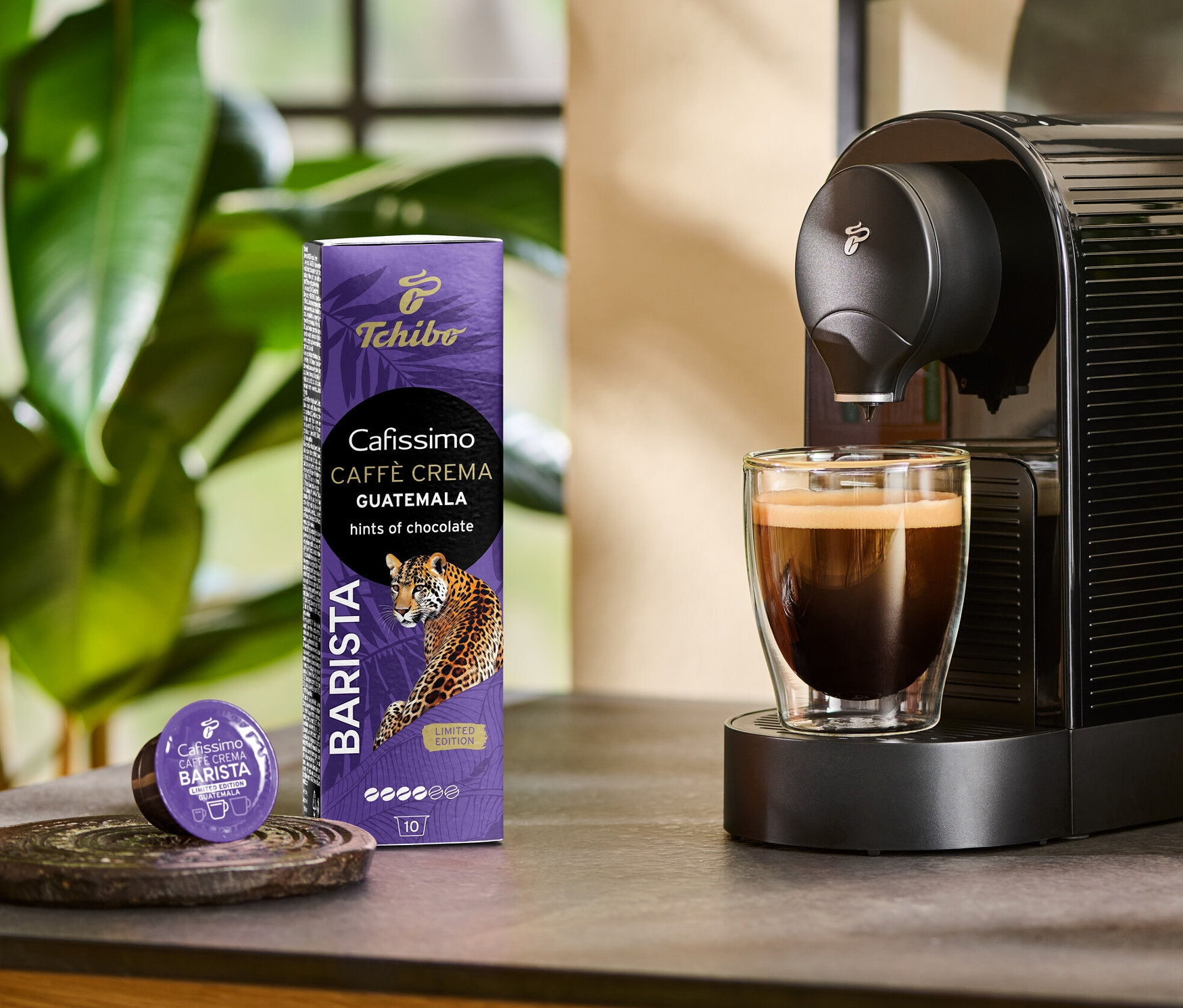 Kahve makinesi bir bardağa Cafissimo BARISTA Caffè Crema Guatemala hazırlıyor. Yanında 10 kapsüllük bir paket ve bir kapsül duruyor.