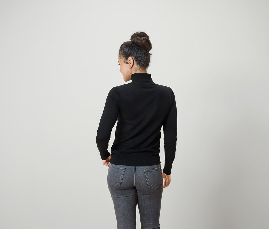 Saçları topuz yapılmış, siyah balıkçı yaka ve gri kot pantolon giyen bir kadının arka görünümü.