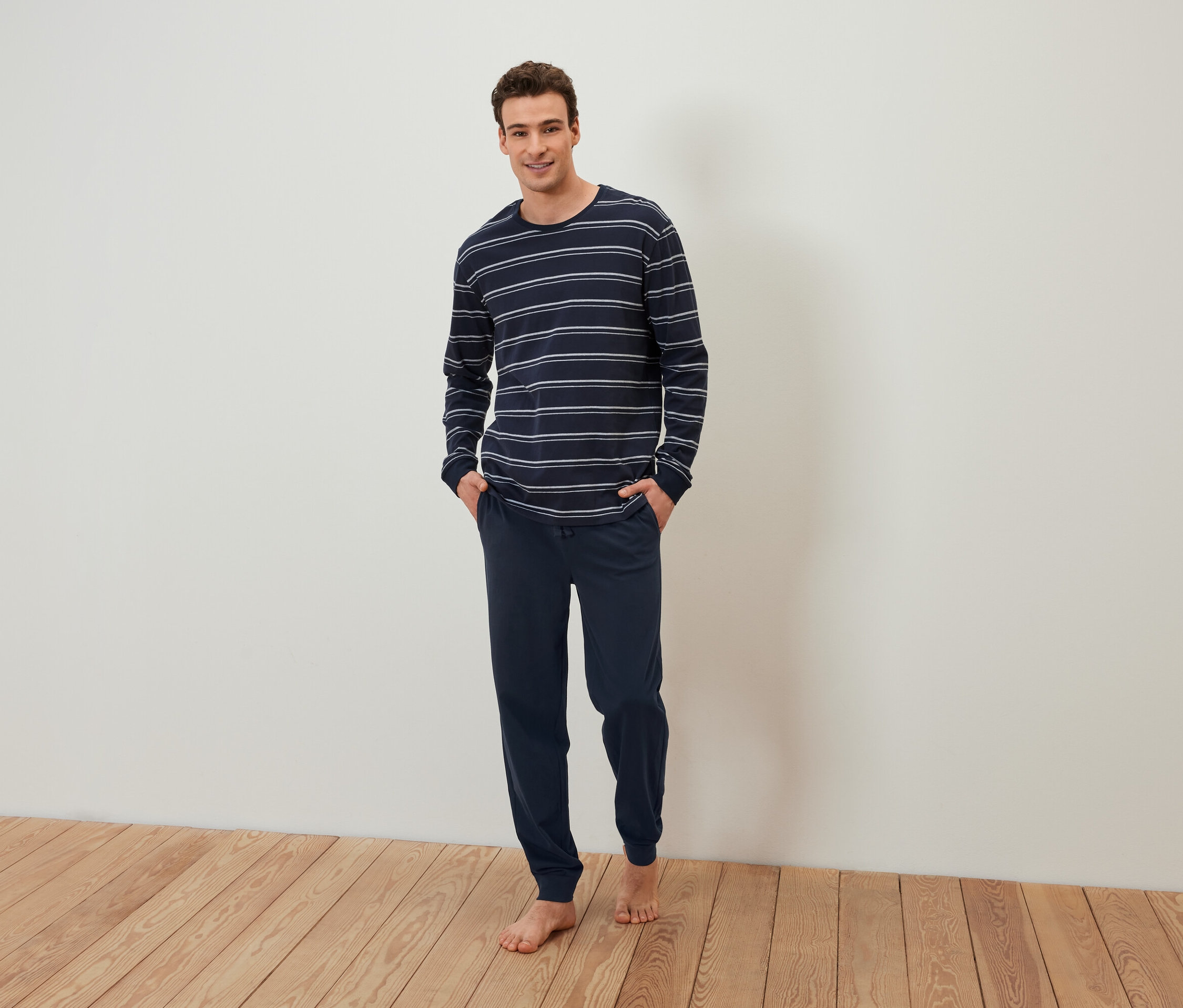 Çıplak ayaklı bir adam, lacivert çizgili bir pijamanın ceplerinde elleriyle duruyor.
