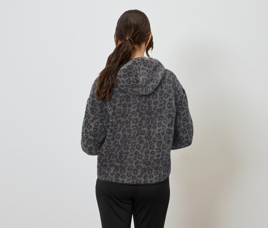 Sırtı kameraya dönük bir kadın, hayvan desenli gri bir kapüşonlu sweatshirt ve siyah pantolon giyiyor.