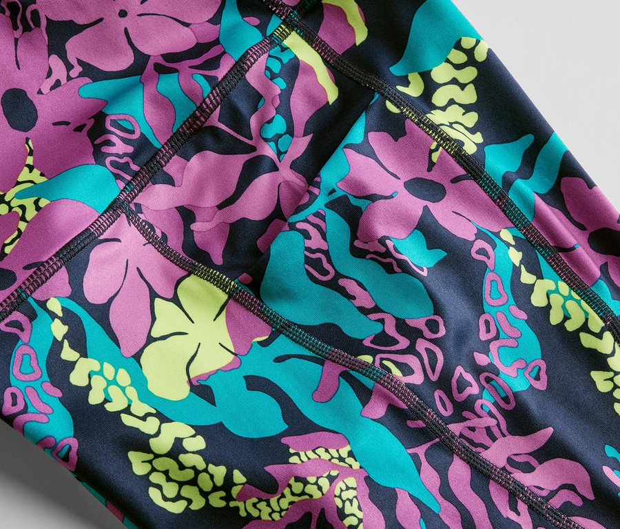 Pembe, turkuaz ve sarı renklerde çiçek ve yaprakların tümü baskılı 3/4 spor taytın yakın çekimi.