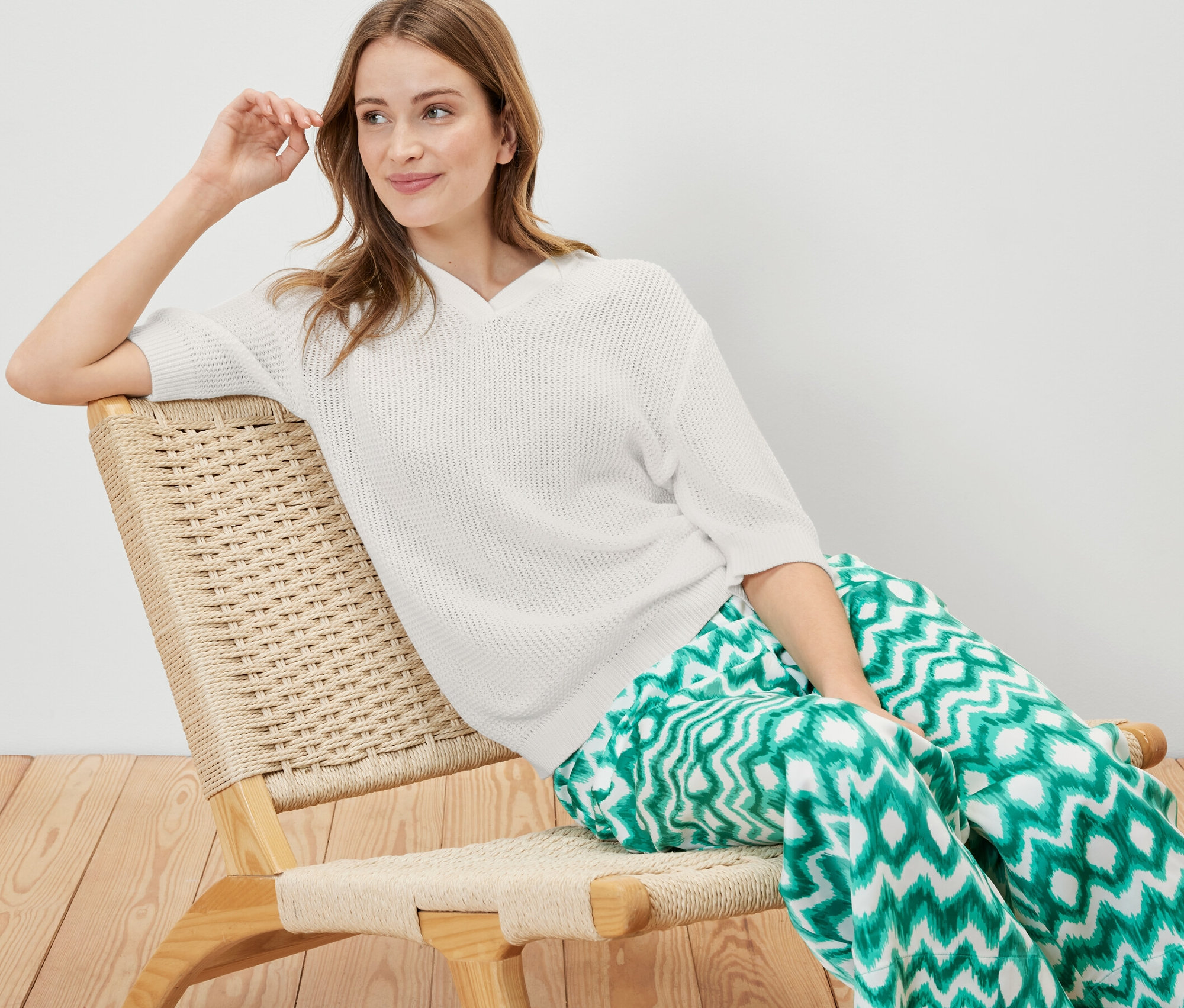 Kadın koltukta oturuyor ve yazlık örme kazak giyiyor.