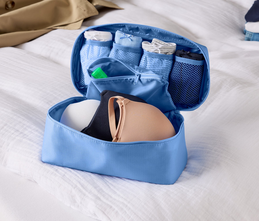 Beyaz bir çarşaf üzerinde sütyen ve iç çamaşırlarıyla açık, açık mavi renkli bir bagaj düzenleyici.
