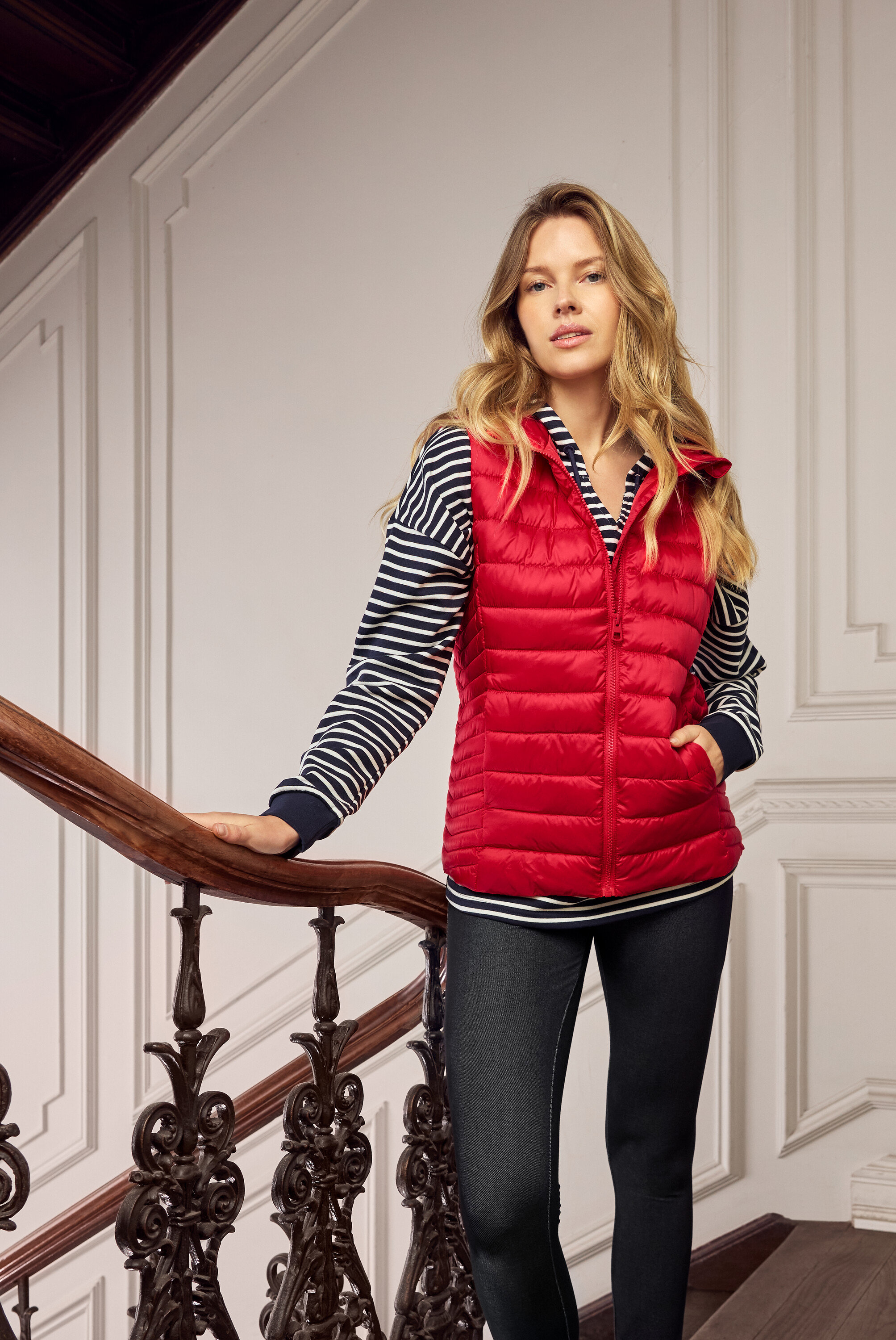 Merdivende kırmızı şişme yelek, lacivert-beyaz çizgili üst ve koyu renk kot pantolon giyen sarışın kadın.