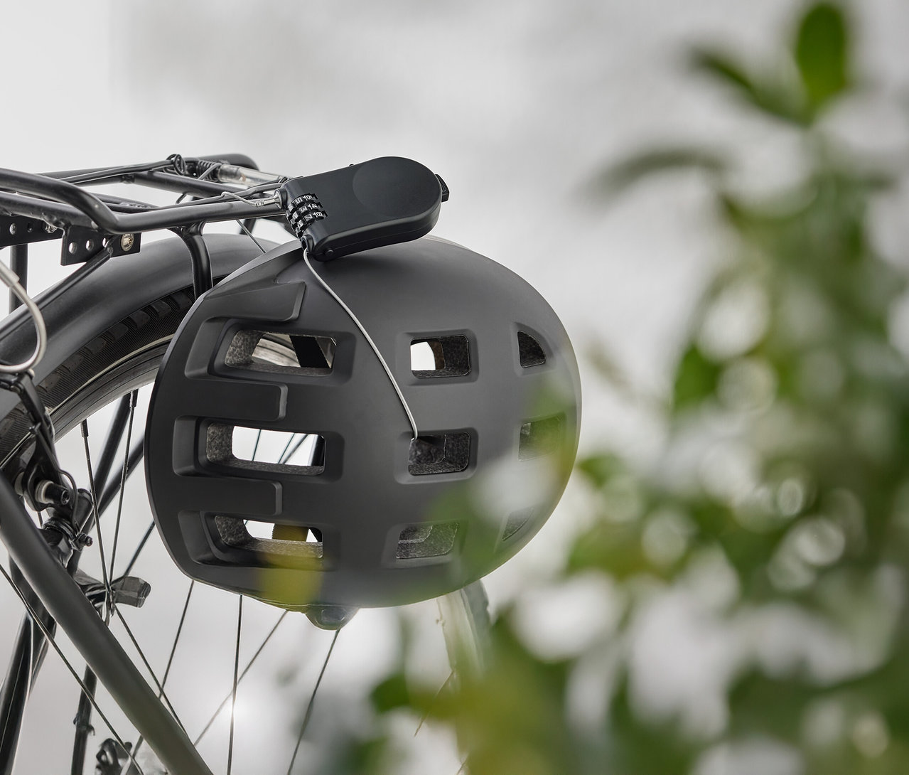 Siyah bir bisiklet kaskı, bisiklet bagajında şifreli bir kilitle asılı duruyor.