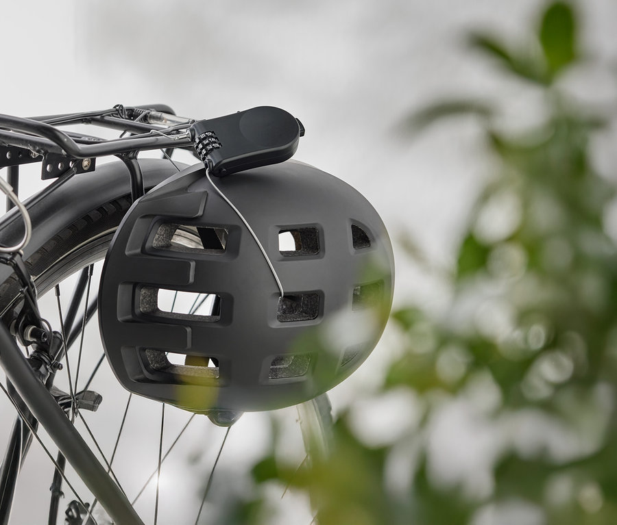 Siyah bir bisiklet kaskı, bisiklet bagajında şifreli bir kilitle asılı duruyor.