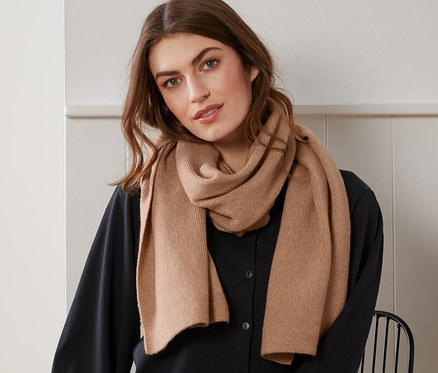 Kadın oturuyor ve kırçıllı bej örgü atkı takıyor.