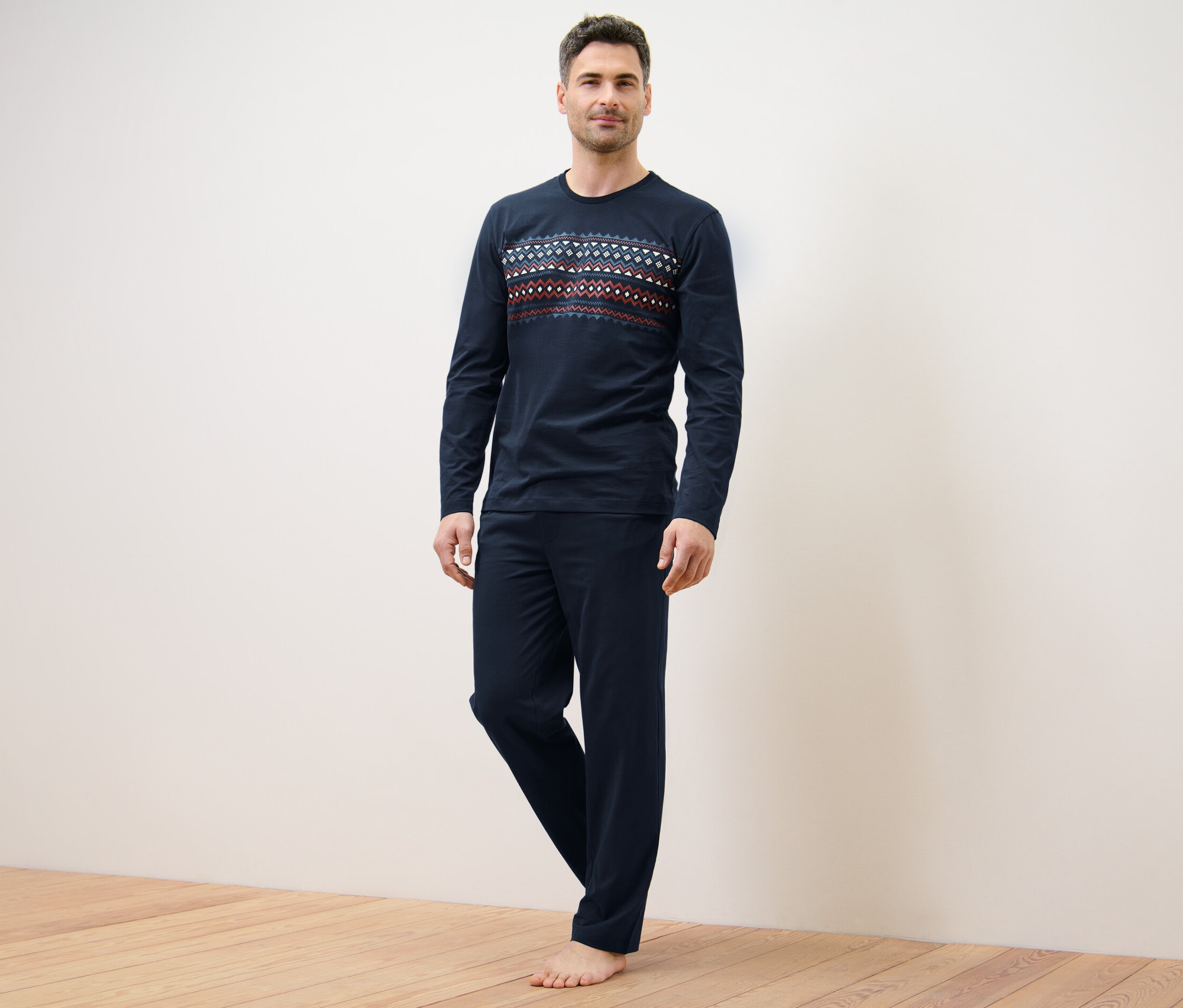 Adam ayakta duruyor ve lacivert bir pijama takımı giyiyor.