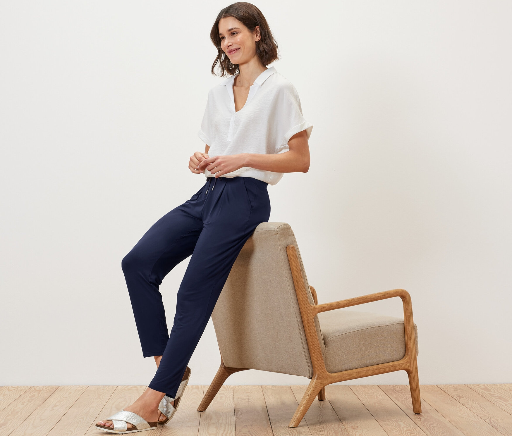 Bir kadın sandalyede oturuyor ve lacivert jarse pantolon giyiyor.