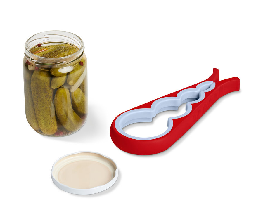 Bir kavanoz salatalık turşusu, bir kapak ve kırmızı bir kavanoz ve şişe açacağı yan yana duruyor.