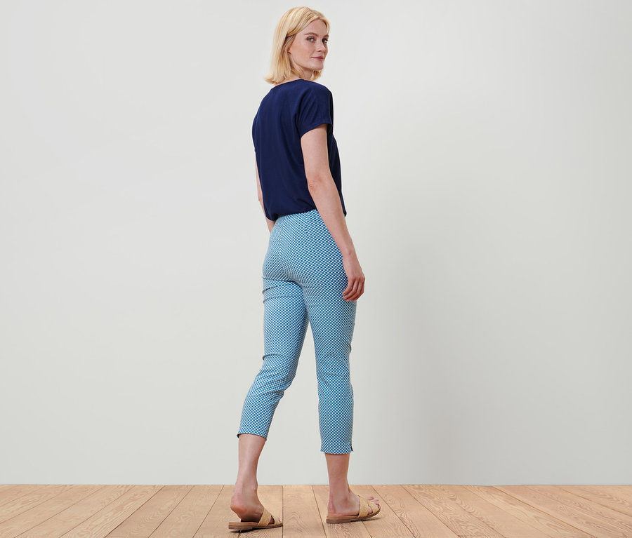 Kadın omzunun üzerinden bakıyor, mavi bir tişört ve tamamı baskılı 7/8 streç pantolon giyiyor.