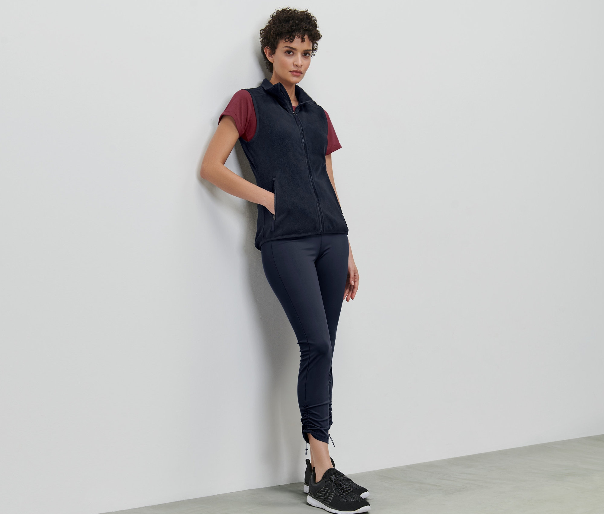 Duvara yaslanmış bir kadın polar yelek giyiyor